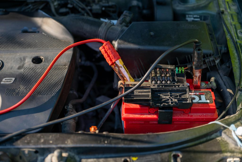 durée de vie batterie golf 7 gte, Close-up of a car battery with attached jumper cables in an engine bay.